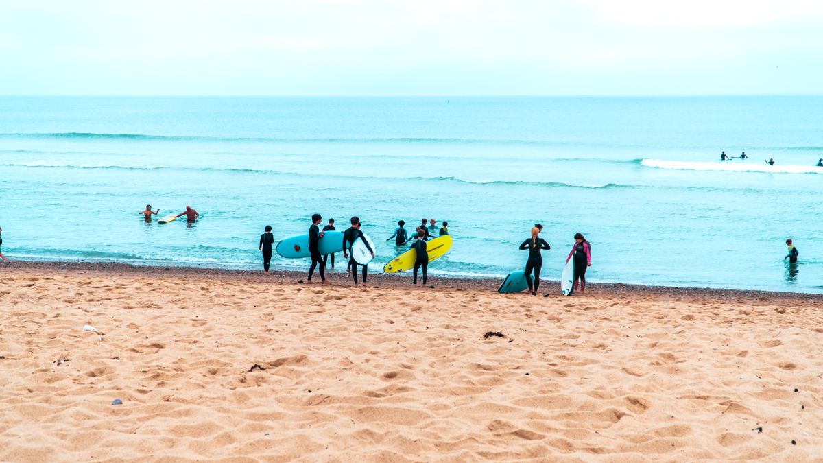 Students heading into the ocean with surfboards at YFC Surf Day